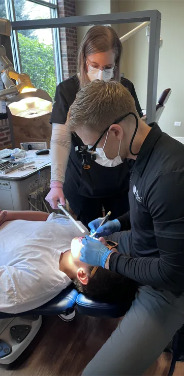 Dr. Daniel Wright examining and adjusting a patient's braces with the help of a staff member